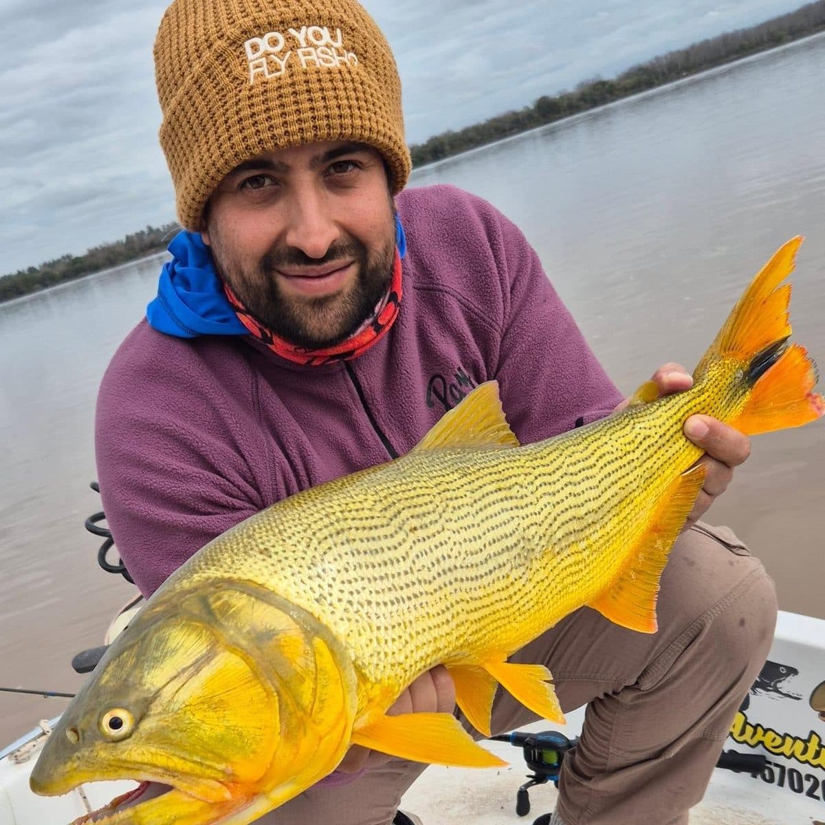 Un pescador con gorro de lana muestra un dorado brillante arriba de la lancha