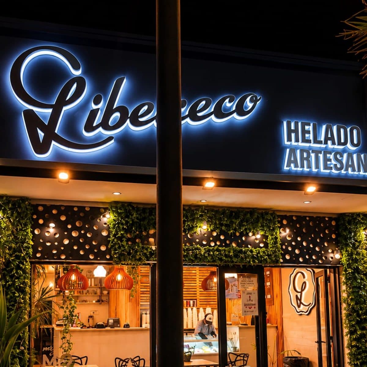 La fachada de noche, con el cartel de neón blanco 'Libereco' encendido sobre la vidriera y guirnaldas de luces entre la hiedra de la entrada