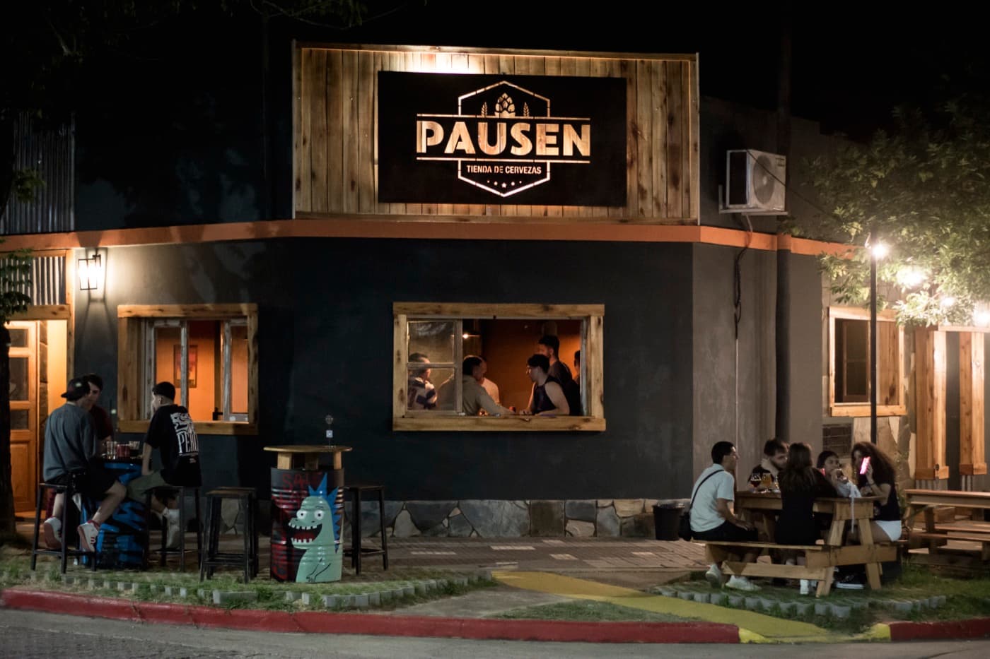 Frente de Pausen de noche, con el cartel iluminado y gente en las mesas de la vereda