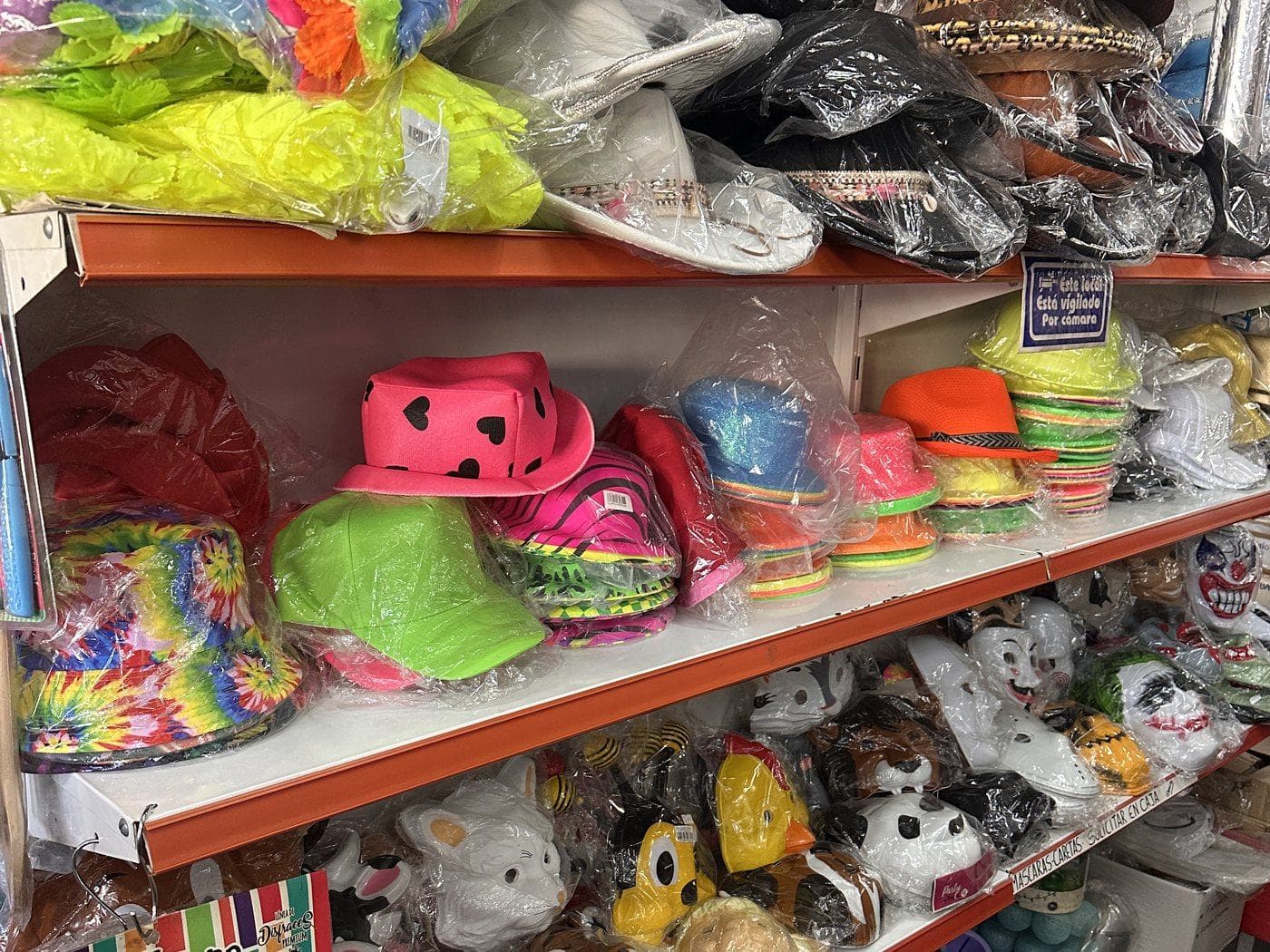 Un estante con sombreros y gorros de colores flúo, y caretas de animales en el estante de abajo
