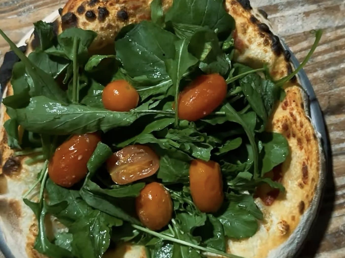 Una pizza de borde tostado con rúcula fresca y tomates cherry por encima