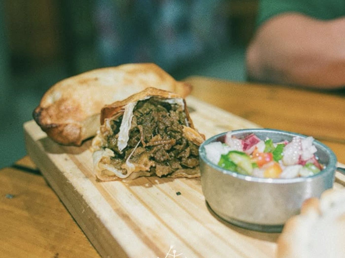 Una empanada de osobuco abierta al medio, con la carne desmechada a la vista y un bowl de salsa criolla al lado