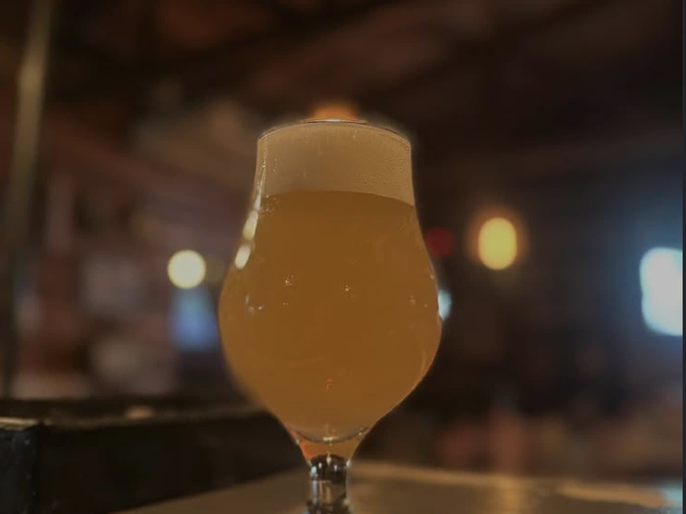 Una copa de cerveza tirada, turbia y con espuma, sobre la barra de madera del Tap