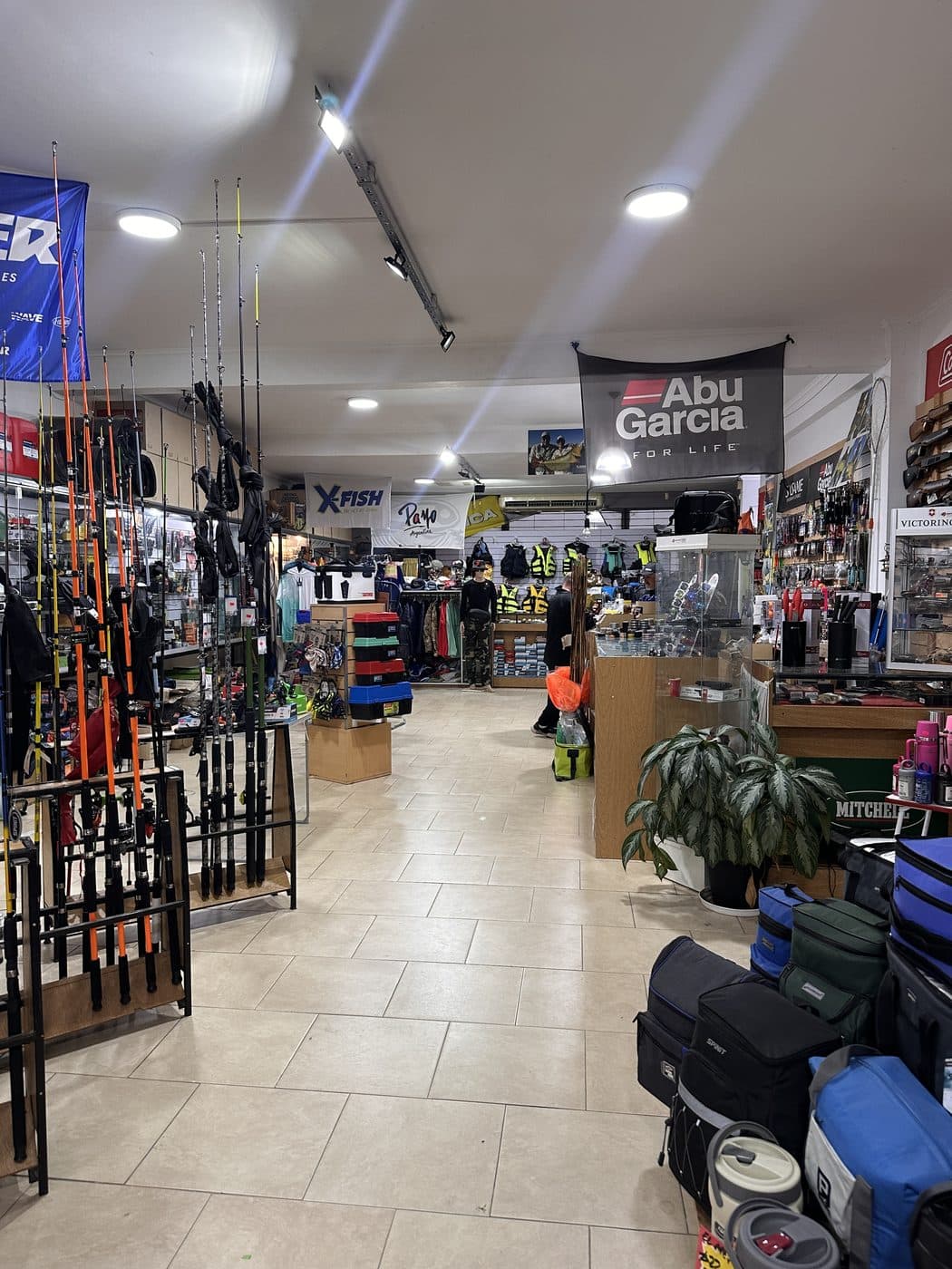 El pasillo central del local, con cañas en los percheros de la izquierda y bolsos y conservadoras a la derecha