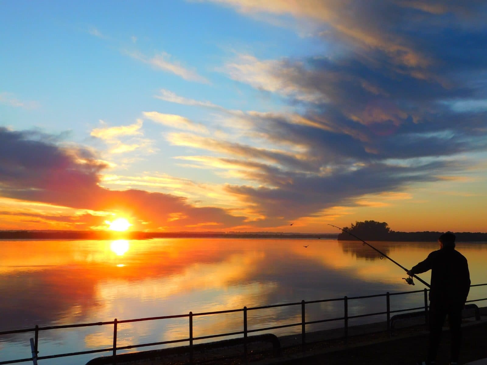Una persona pescando desde la costanera de Colón, con el sol bajo sobre el río Uruguay