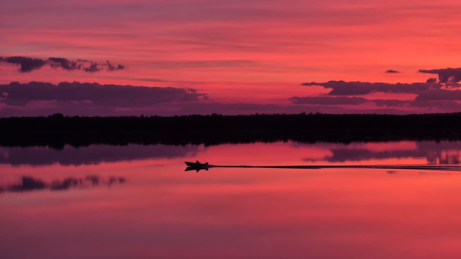 Una lancha navegando el río Uruguay al atardecer, en silueta contra el cielo rosado, en Colón, Entre Ríos